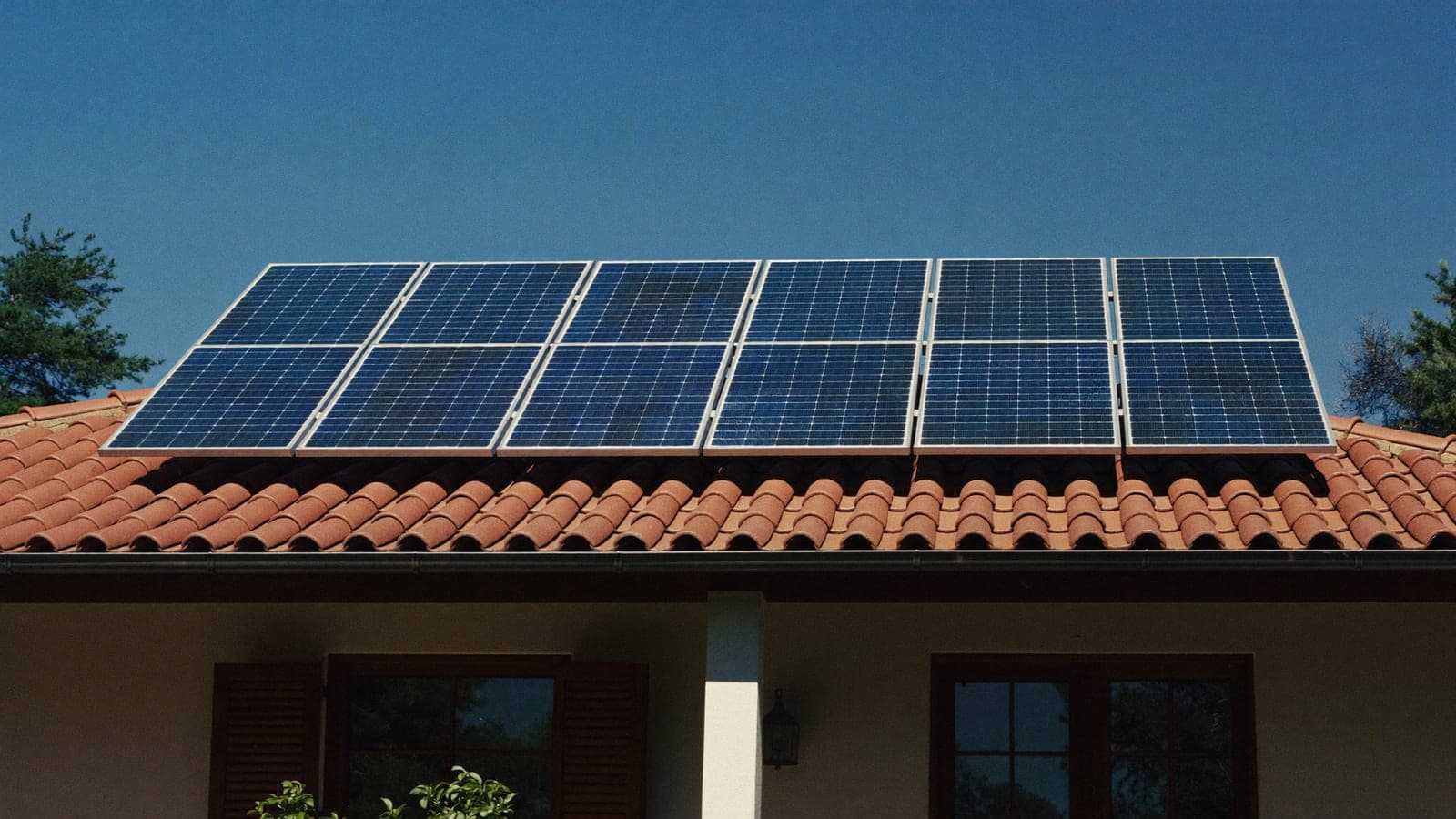 Placas solares fotovoltaicas en el tejado de tejas de una casa mediterránea española bajo el sol intenso del mediodía de agosto.