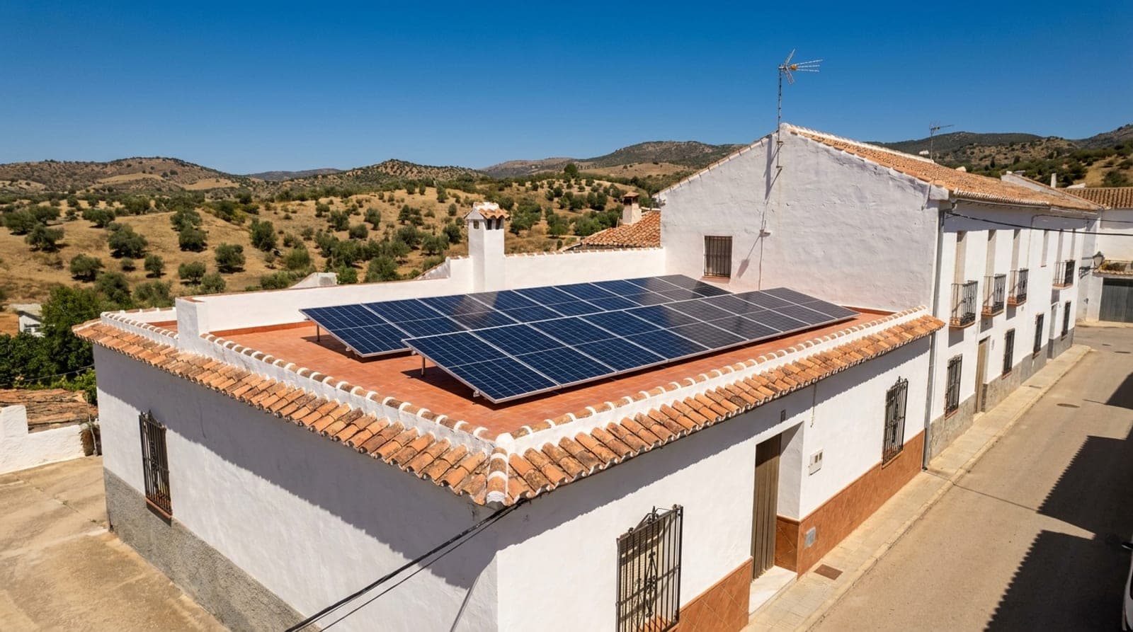 Casa encalada andaluza con placas solares fotovoltaicas en el tejado bajo un cielo azul despejado de verano a mediodía, en un pueblo del sur de España.