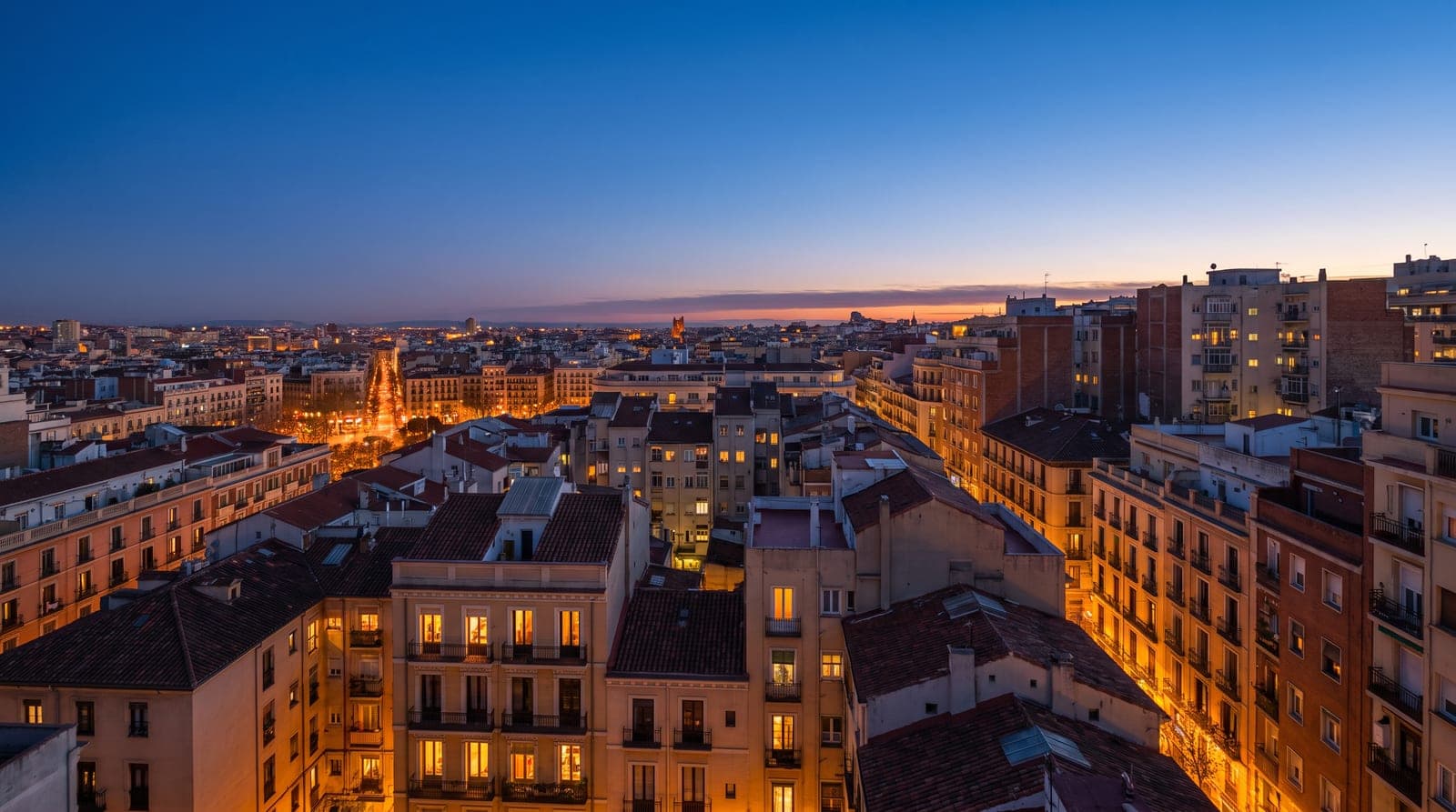 Horizonte de una ciudad española al anochecer con las ventanas de los edificios iluminadas en la hora punta de la tarde