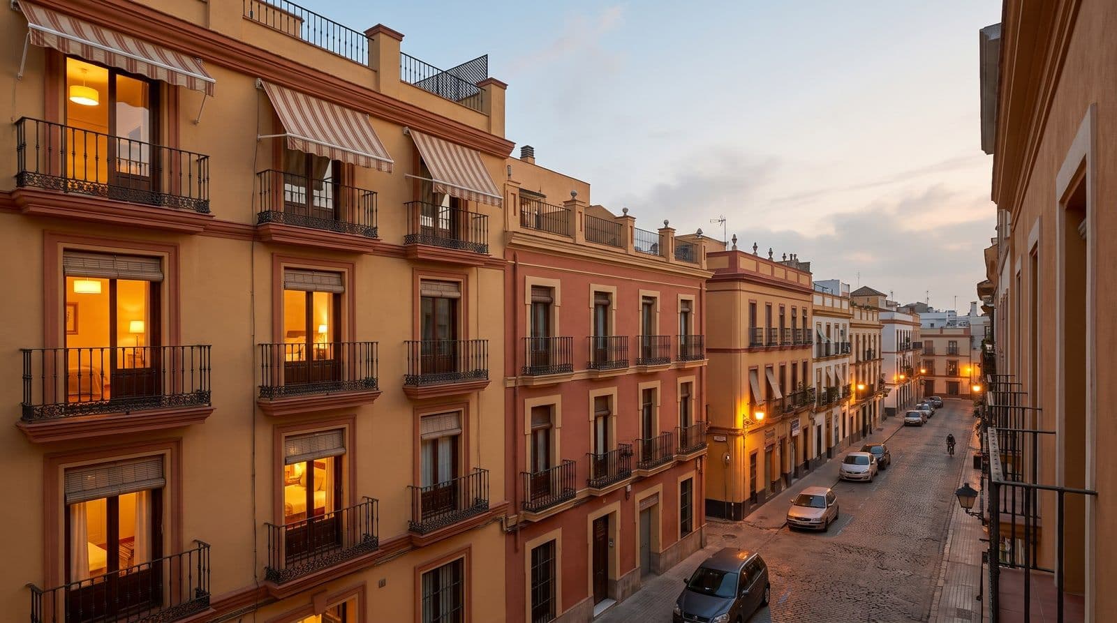 Barrio residencial español al anochecer con las luces de las ventanas encendiéndose en la hora punta de la tarde