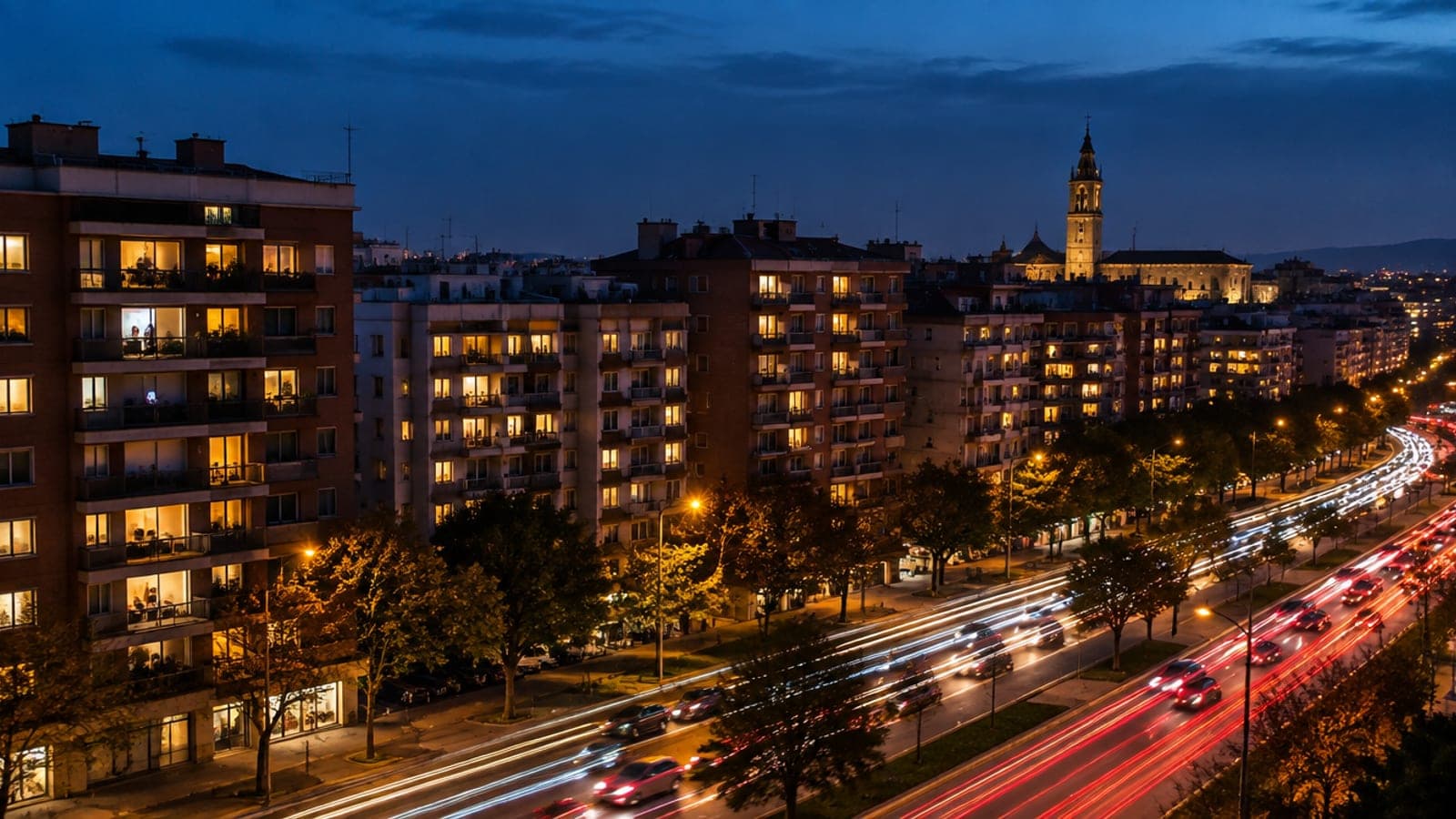 Barrio de una ciudad española de noche en hora punta, con cientos de ventanas iluminadas y una avenida con estelas de luz de los coches